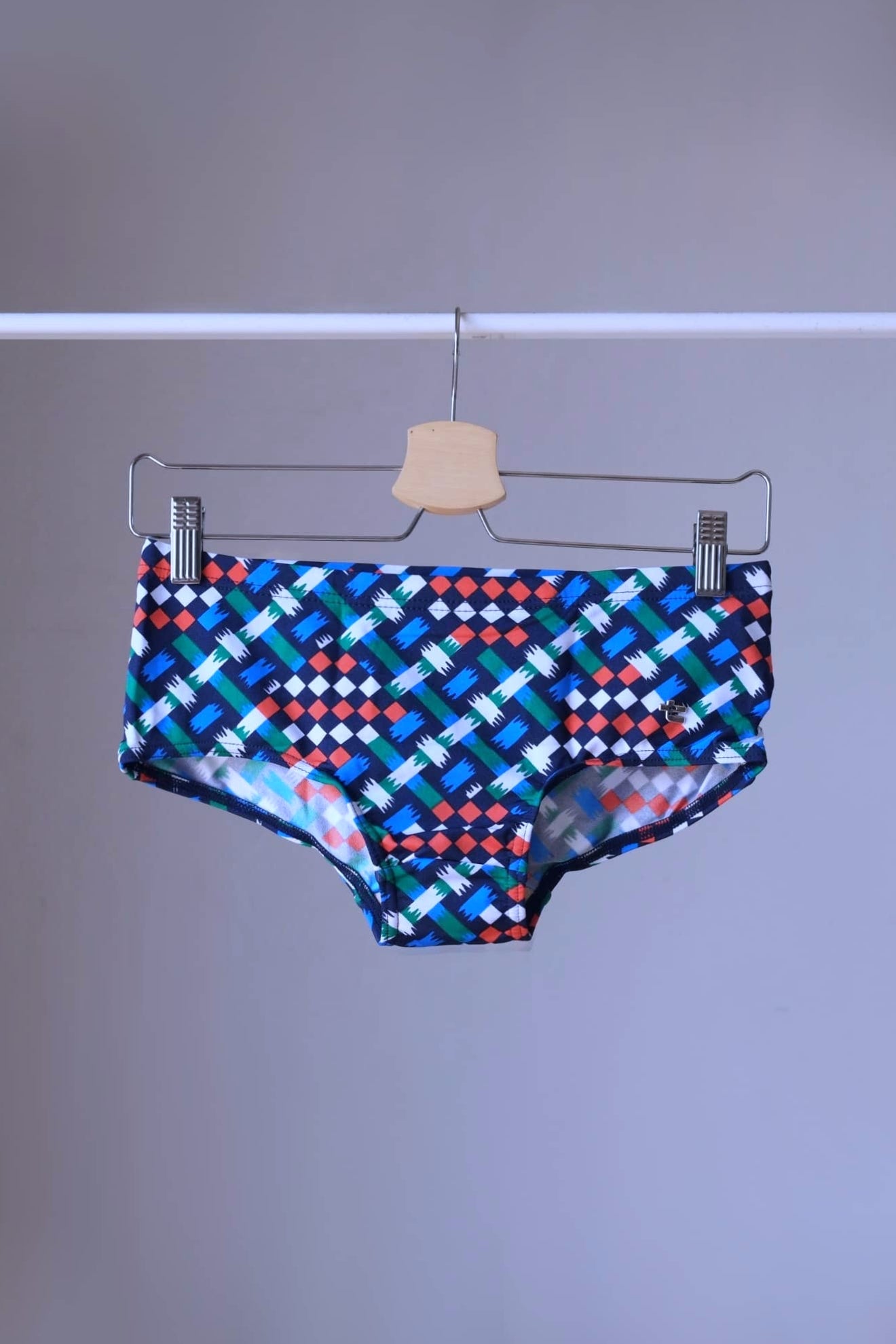 swim briefs in a geometric pattern of blue,  green, white, red on a hanger