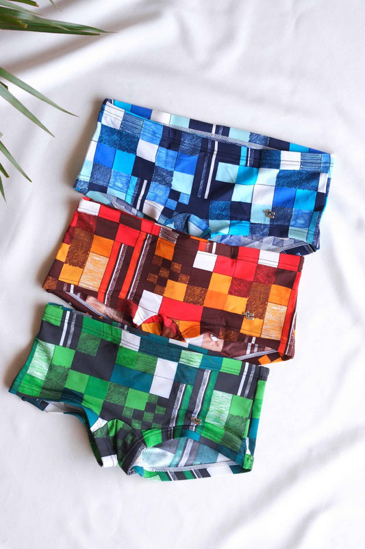 Three pairs of Tropic vintage swim briefs, each with a different checkered pattern. The patterns are in various colors, including blue, green, red, and orange.