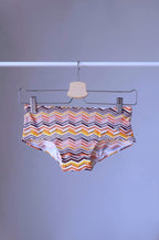 Tropic Vintage swim briefs featuring a brown, orange and yellow chevron pattern, hanging on a hanger.