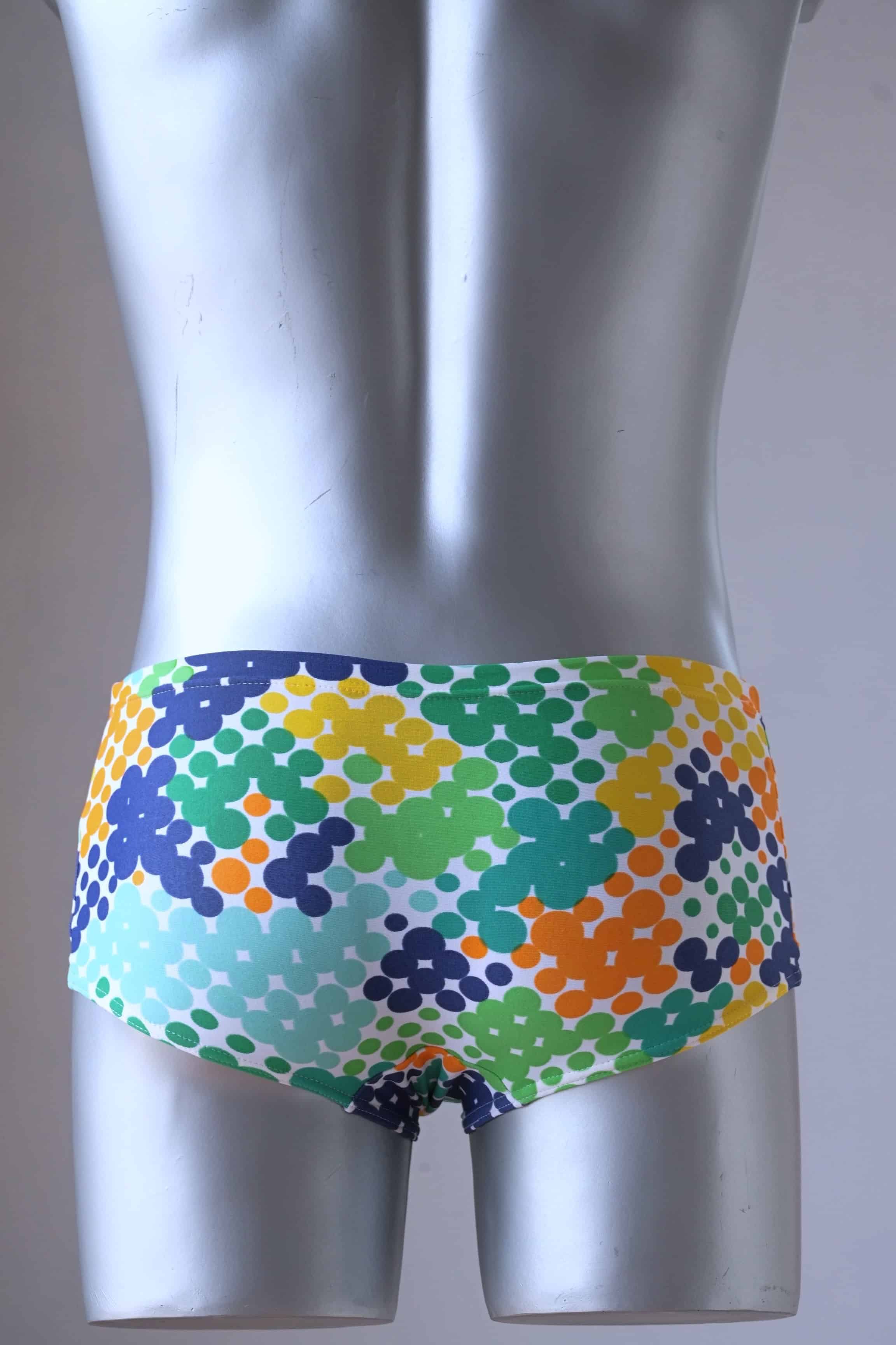 Backside of TROPIC Vintage Retro Dot Print Swim Briefs on a silver mannequin, showcasing the blue-green variant with a vibrant geometric dotted design. The pattern includes shades of green, blue, yellow, and orange dots for a bold, retro look.
