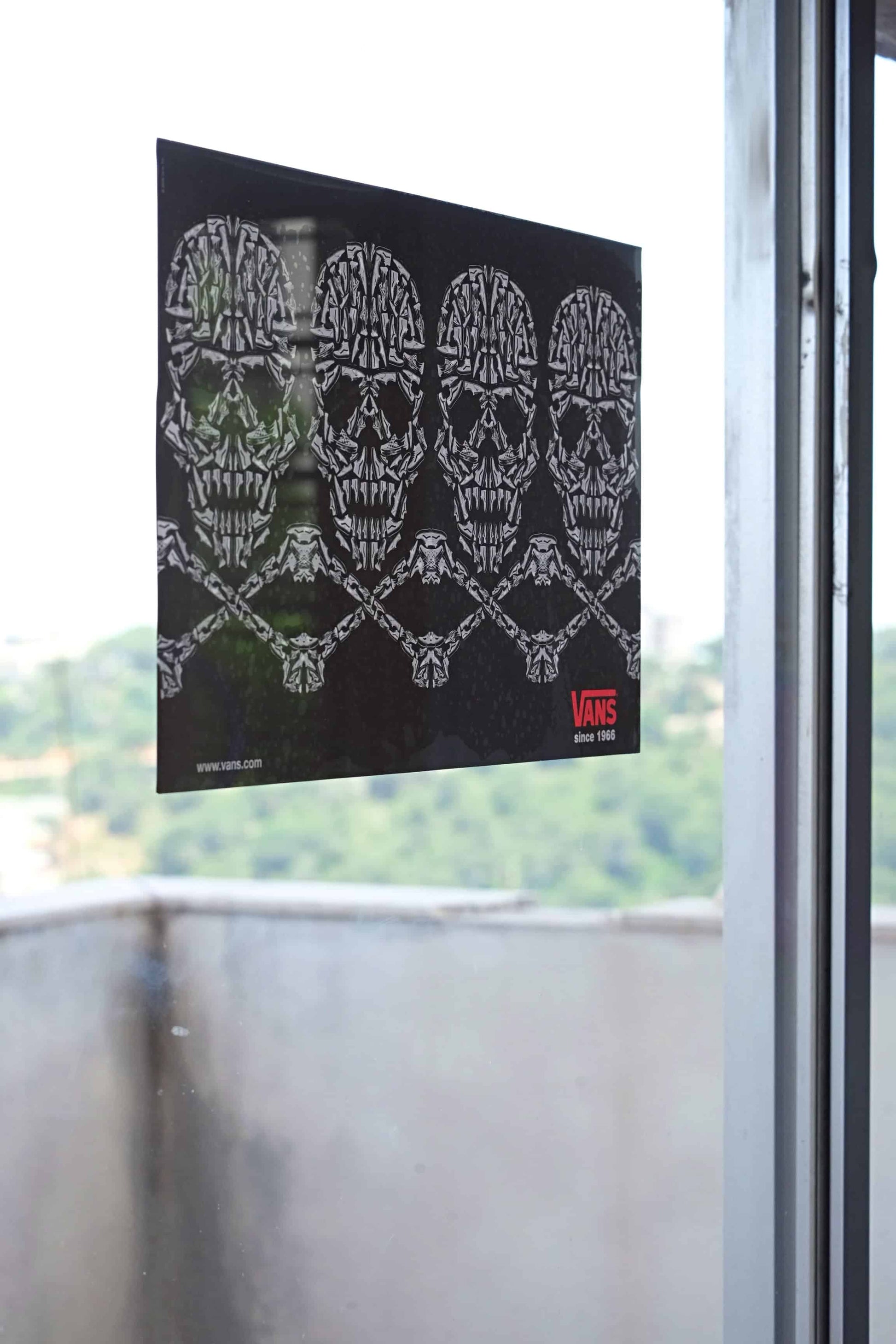 Angled view of a 2008 Vans dealer promo window cling featuring a row of skulls made from Vans sneakers, applied to a glass window with a blurred outdoor background.