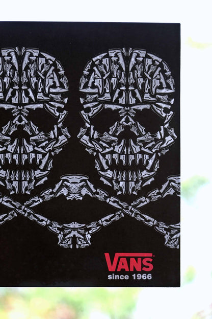 Close view of Vans 2008 static cling window sticker with skulls and crossbones design, made from sneaker illustrations, placed on a clear window with natural light and trees behind.