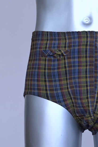 Close view of a vintage late 1950s to early 1960s men's swim brief on a silver mannequin. The brief features a plaid pattern in dark brown, blue, and yellow tones, with a small front flap pocket.