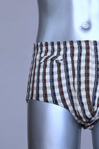 Close view of a vintage late 1950s to early 1960s men's swim brief on a silver mannequin. The brief features a plaid pattern in white, blue, and red, with a small front flap pocket.