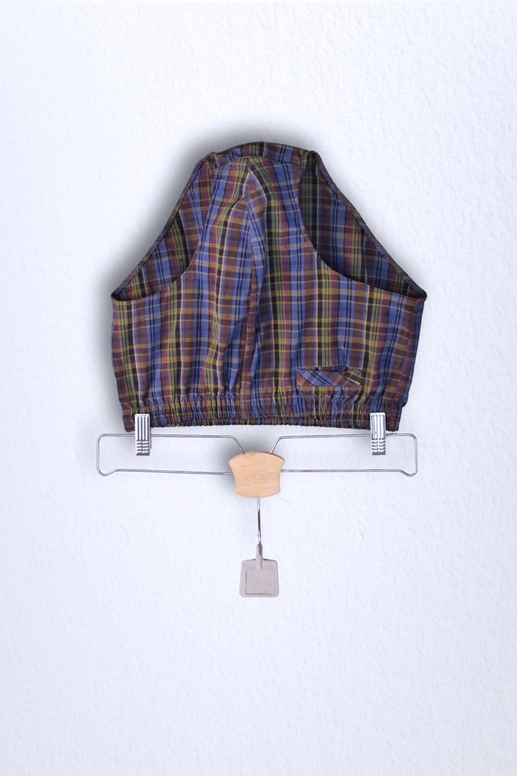 Front view of a vintage late 1950s to early 1960s men's swim brief on a hanger. The brief features a plaid pattern in dark brown, blue, and yellow tones, with a small front flap pocket.