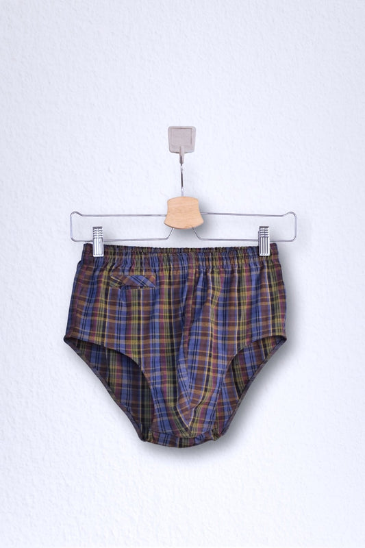 Front view of a vintage late 1950s to early 1960s men's swim brief on a hanger. The brief features a plaid pattern in dark brown, blue, and yellow tones, with a small front flap pocket.