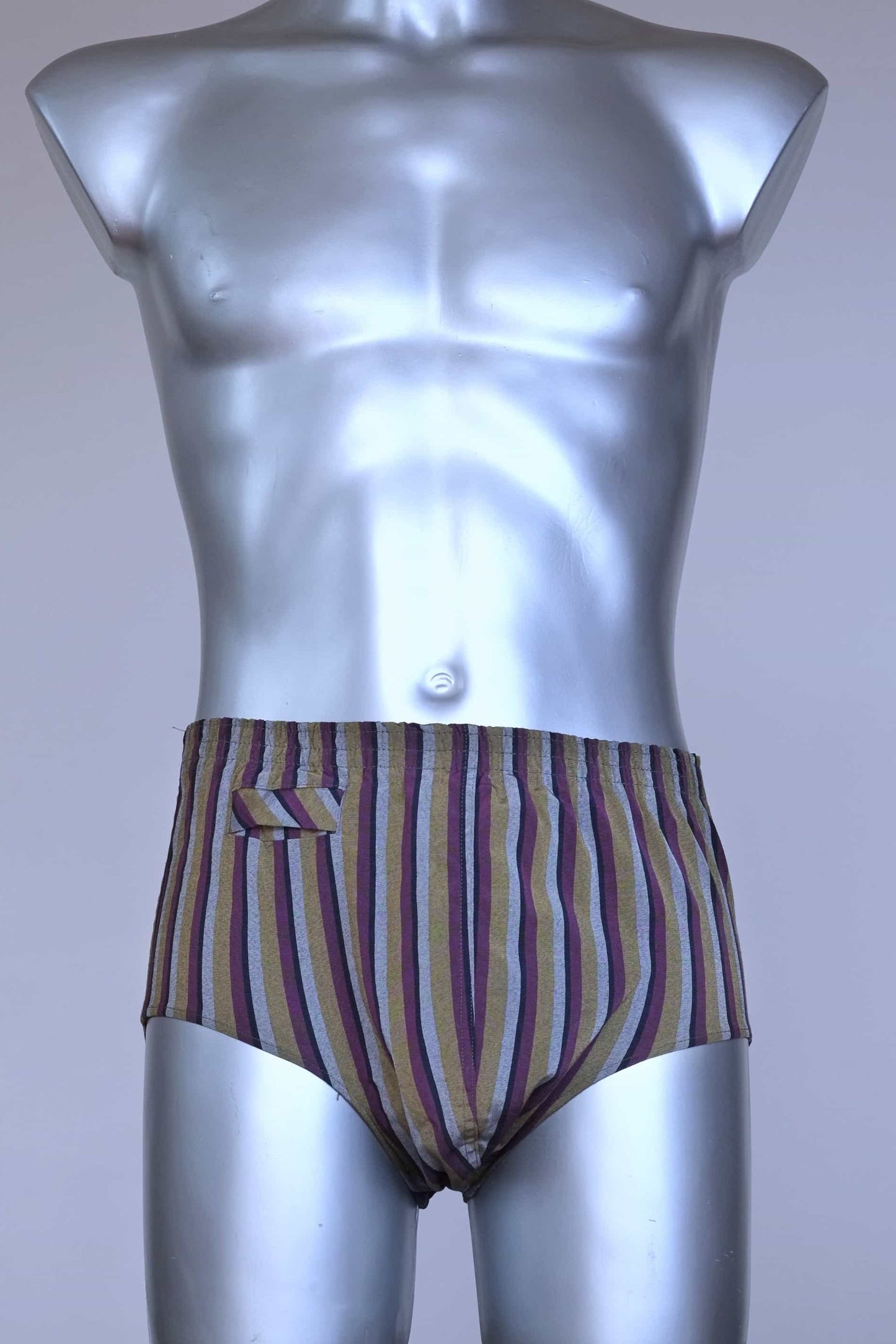 Front view of a vintage late 1950s to early 1960s men's swim brief on a silver mannequin. The brief features vertical stripes in muted brown, grey, and maroon tones, with a small front flap pocket.