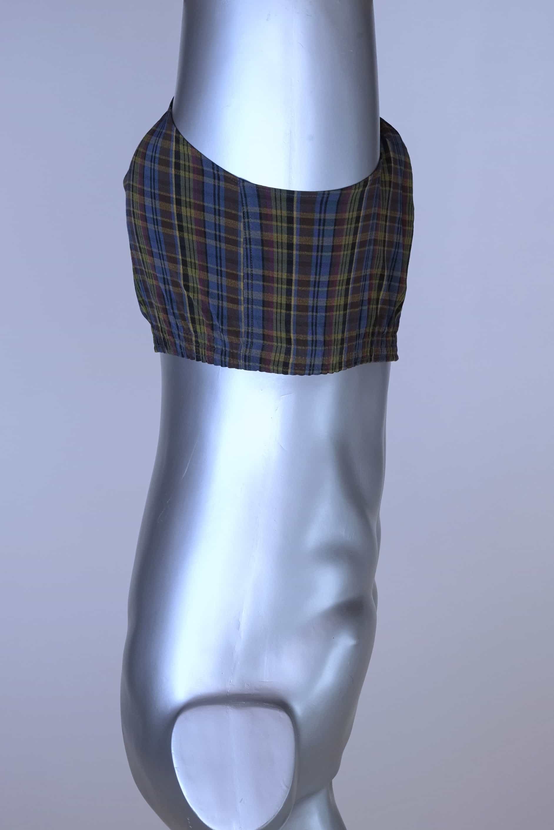 Side view of a vintage late 1950s to early 1960s men's swim brief on a silver mannequin. The brief features a plaid pattern in dark brown, blue, and yellow tones, with a small front flap pocket.