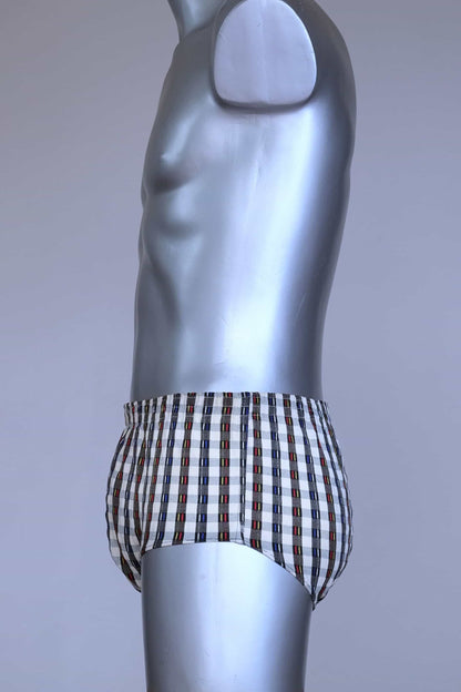 Side view of a vintage late 1950s to early 1960s men's swim brief on a silver mannequin. The brief features a plaid pattern in white, blue, and red, with a small front flap pocket.