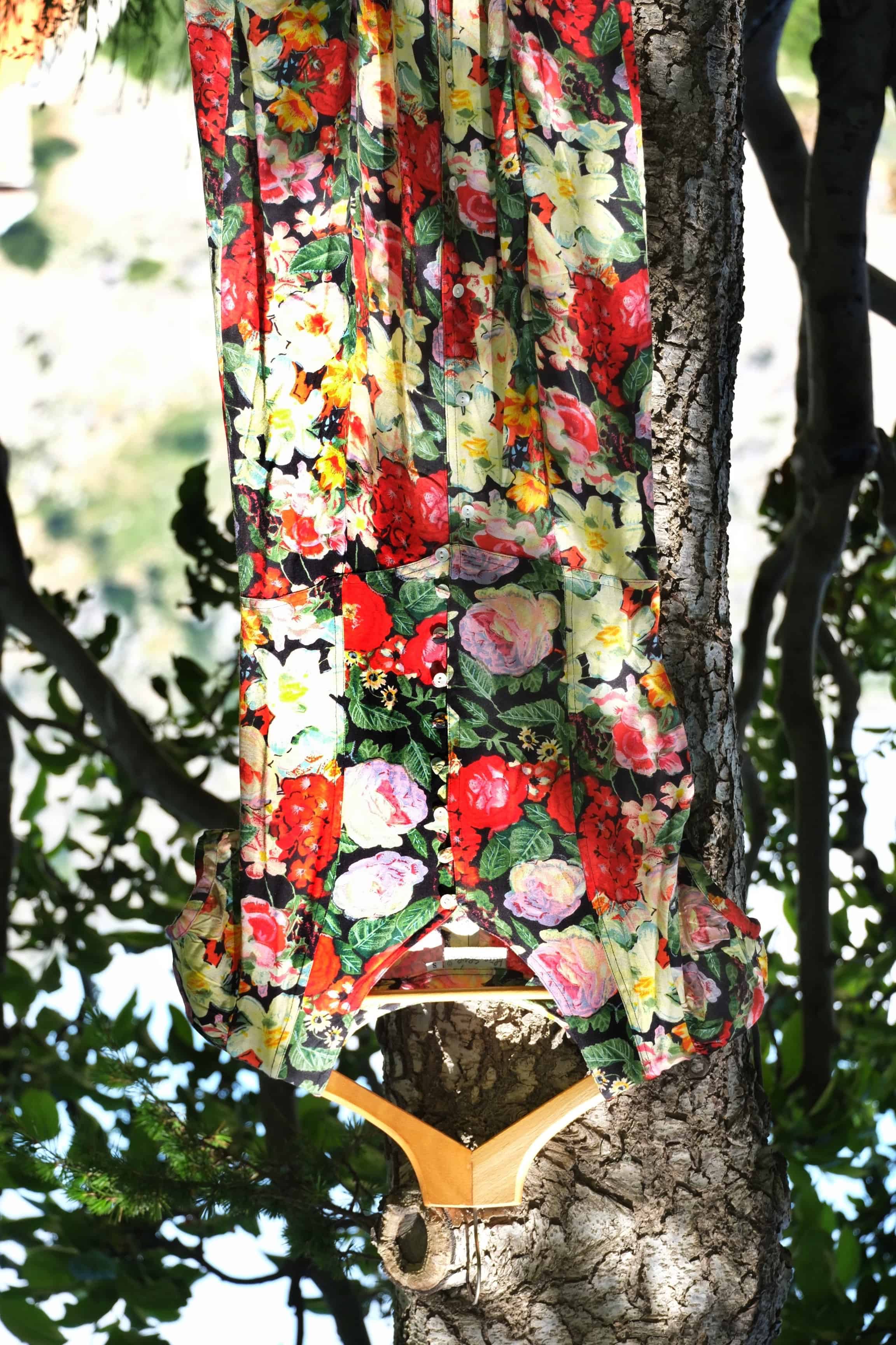 Vintage 90s floral maxi dress with button front, hanging on wooden hanger against tree bark