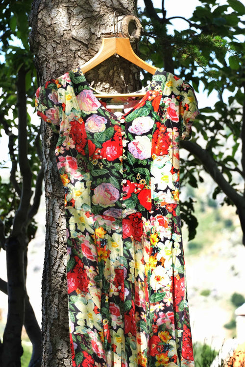 Vintage 90s floral maxi dress with button front, hanging on wooden hanger against tree bark