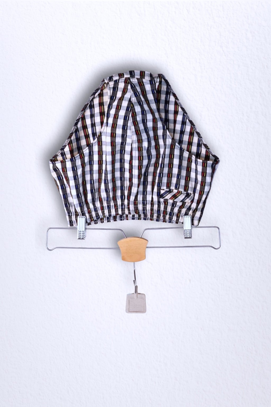 Front view of a vintage late 1950s to early 1960s men's swim brief on a hanger. The brief features a plaid pattern in white, blue, and red, with a small front flap pocket.