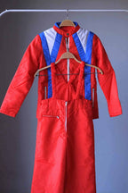 Full view of a two-piece retro ski suit by Warmia featuring a vibrant red insulated jacket with blue geometric details and high-waisted red bib overalls with ruffled elastic straps.