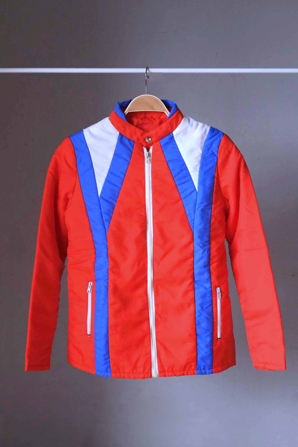 Full view of the jacket from a two-piece retro ski suit by Warmia featuring a vibrant red insulated jacket with blue geometric details.
