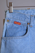 Close-up of WRANGLER vintage 90s light wash jeans front pocket featuring a red logo tab and classic copper rivet.