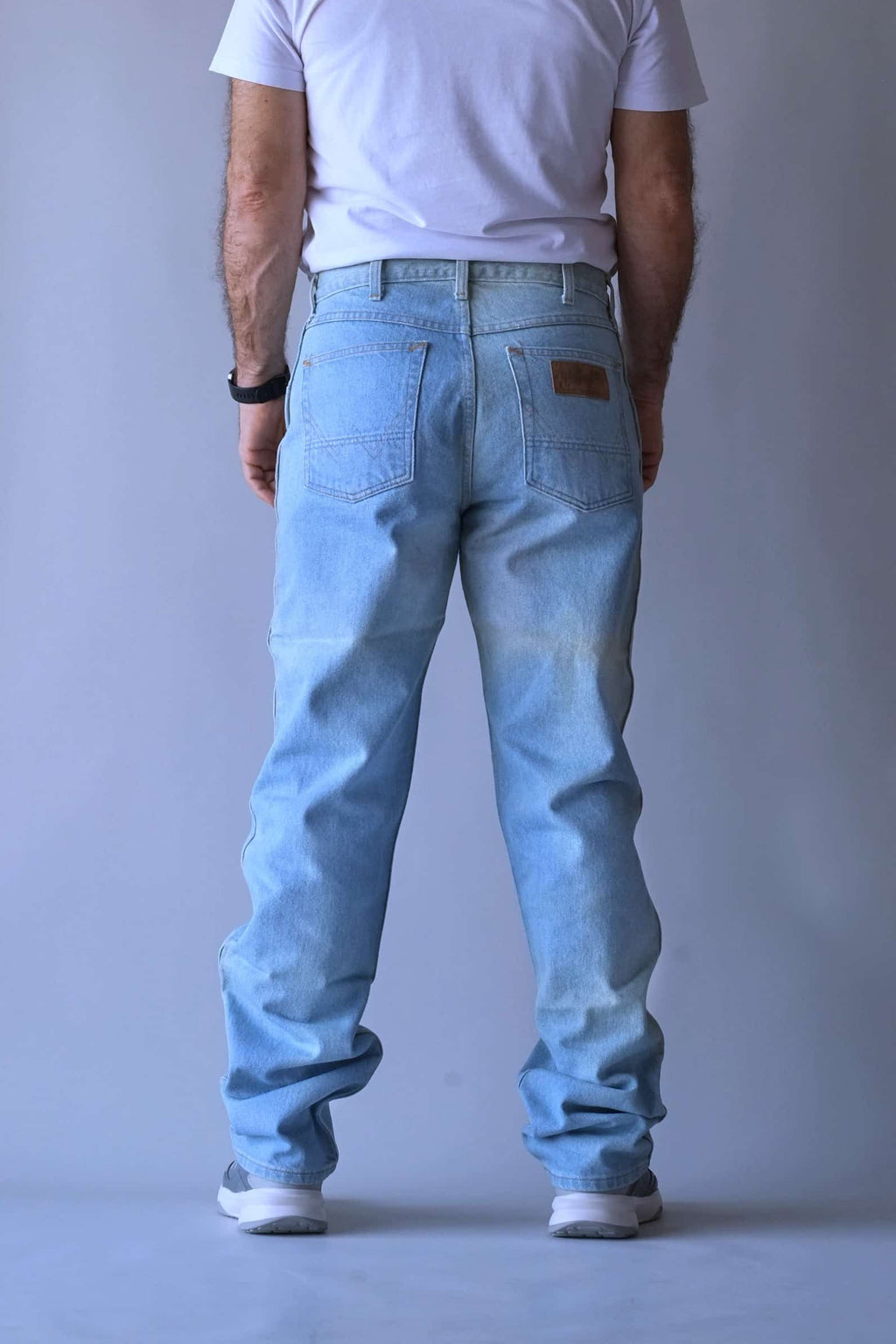Rear view of a man wearing WRANGLER vintage straight leg jeans in a light wash, showcasing the fit and leather logo back patch.