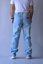 Rear view of a man wearing WRANGLER vintage straight leg jeans in a light wash, showcasing the fit and leather logo back patch.