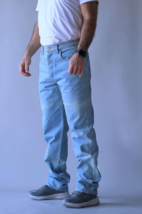 Front-facing lifestyle shot of a man wearing 90s WRANGLER light wash western jeans with a white t-shirt and grey sneakers.