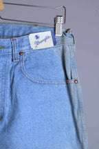 Close-up of vintage WRANGLER light wash jeans waistband with original price tag and visible storage discoloration along the side fold.