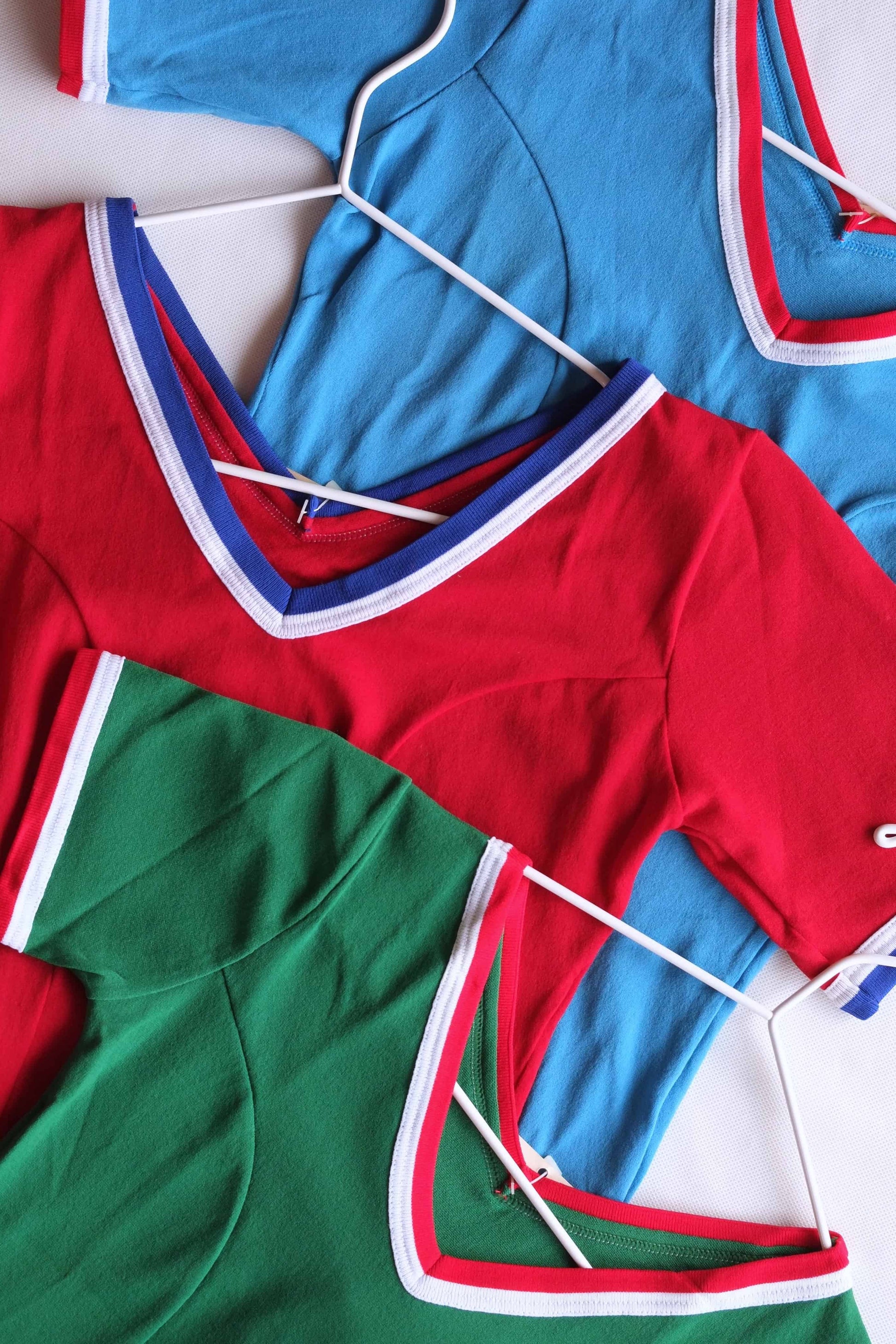 Cropped view of the V-neck and collar trim on three vintage 70s leotards in red, green, and blue.