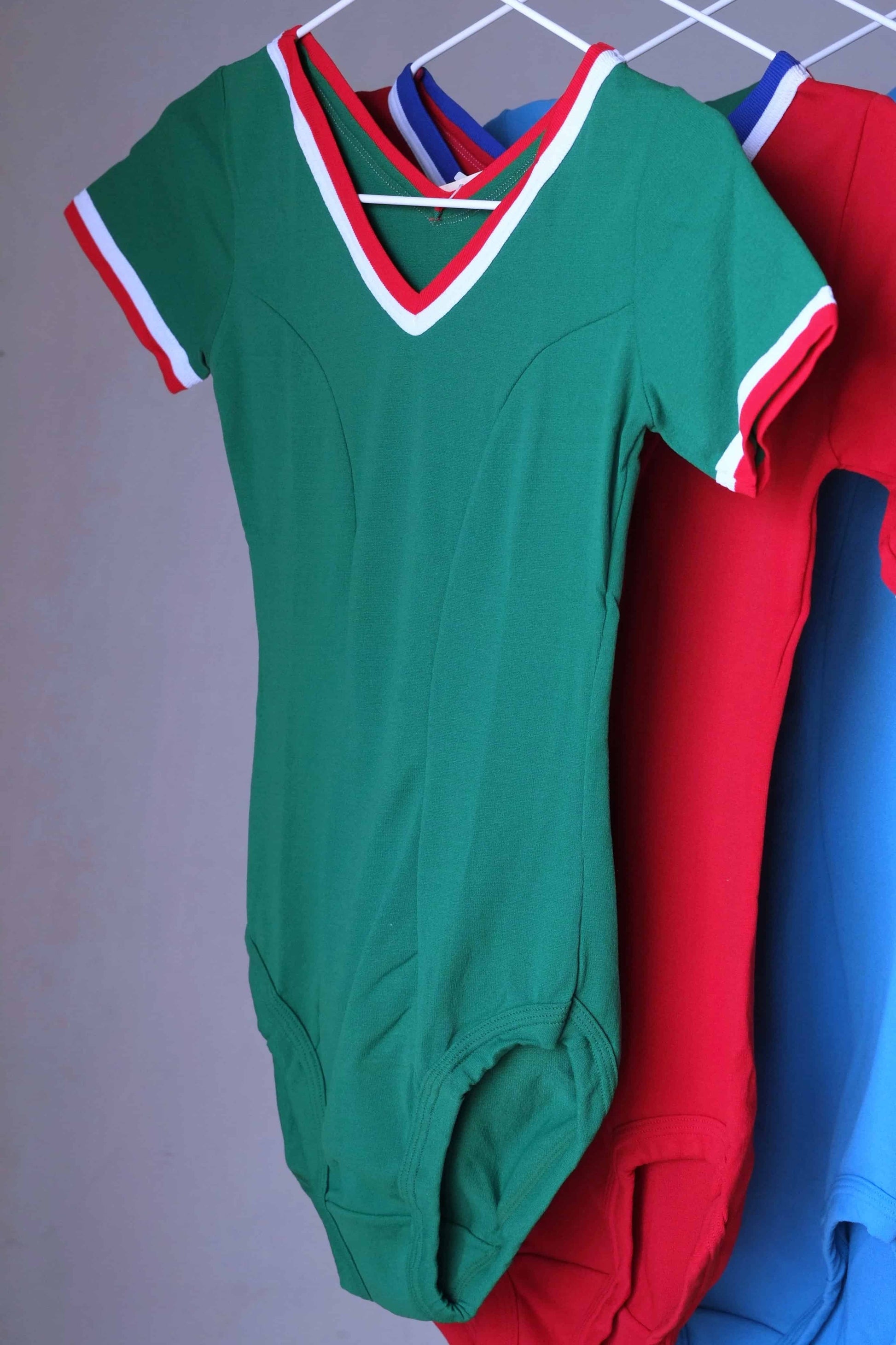 Green vintage 70s short sleeve leotard with white and red trim, hanging on a rack.