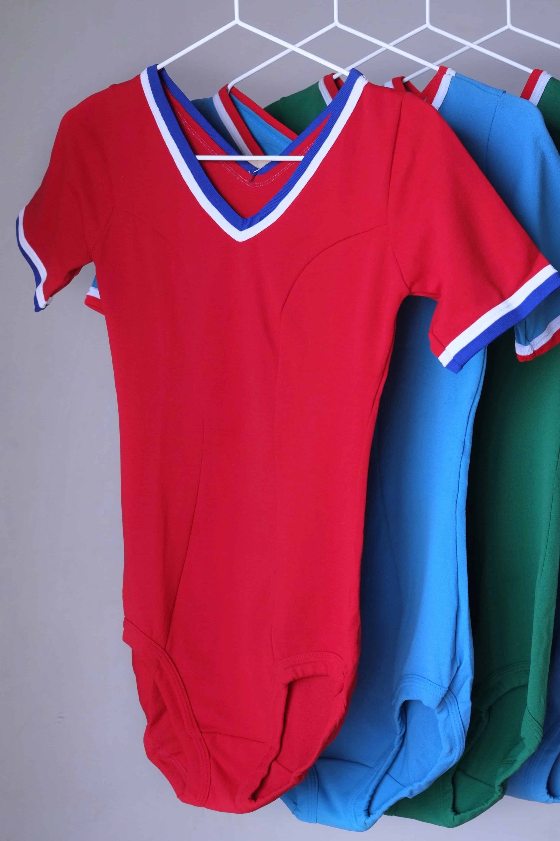 Red vintage 70s short sleeve leotard with white and red trim, hanging on a rack.