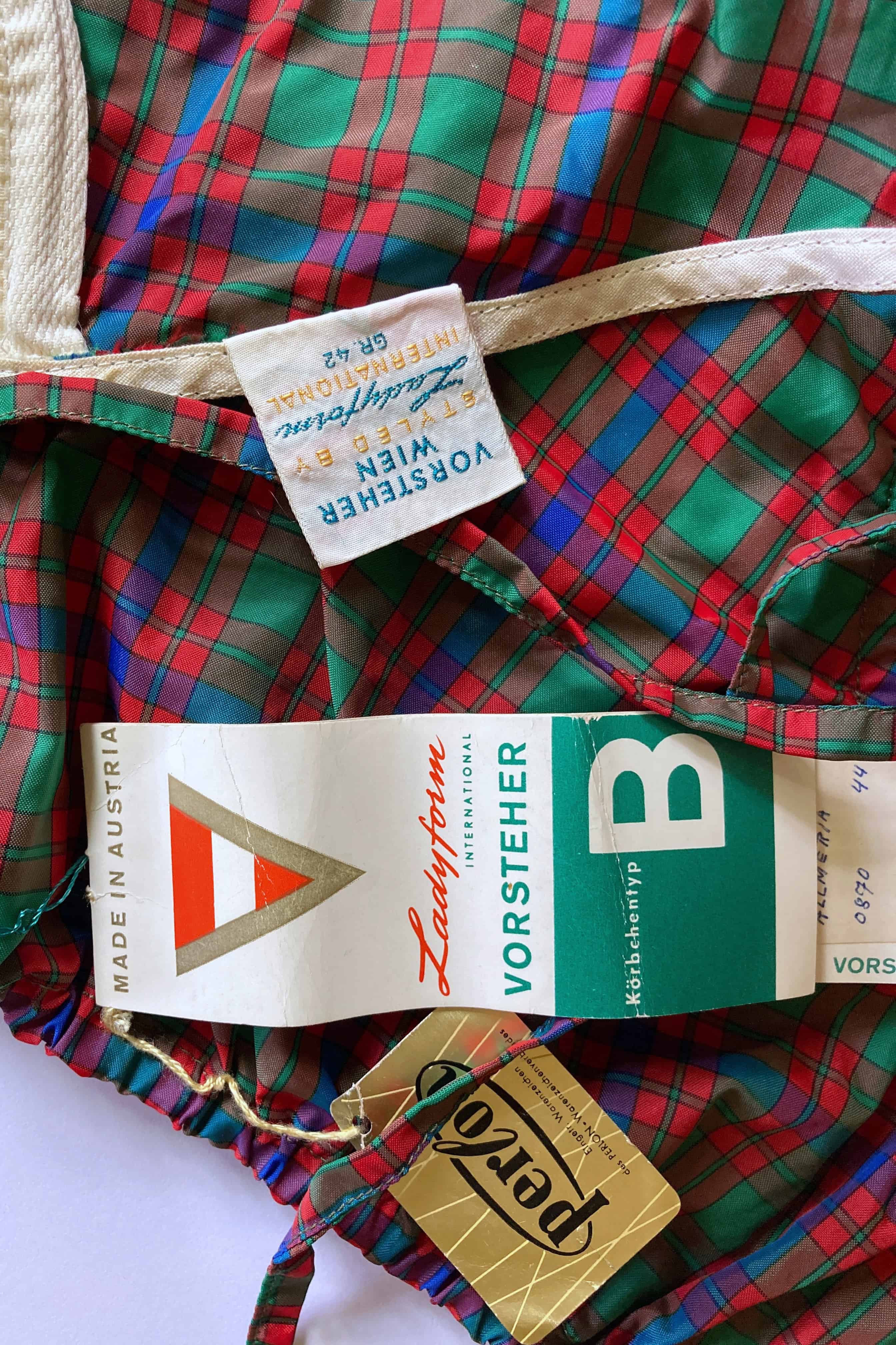 Close-up of the interior Vorsteher Wien Ladyform fabric label showing size 42, displayed next to paper hang tags on tartan plaid material.