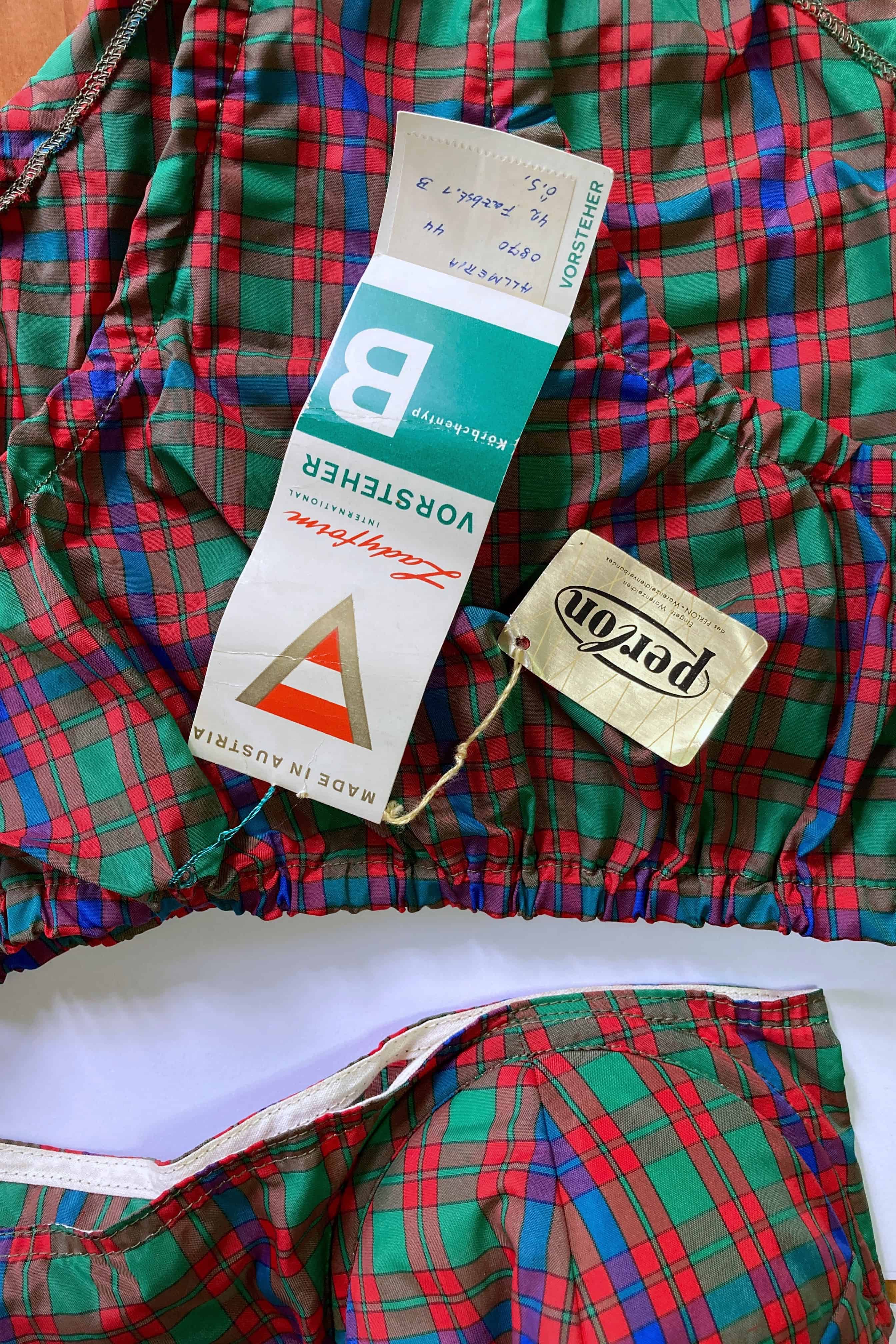Flat lay close-up of original vintage paper hang tags for Vorsteher Ladyform size B and Perlon attached to tartan plaid bikini bottoms.