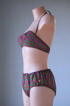 Side profile view of a vintage red and green plaid bikini set on a mannequin, showcasing the cup shape, halter tie, and side hip coverage.
