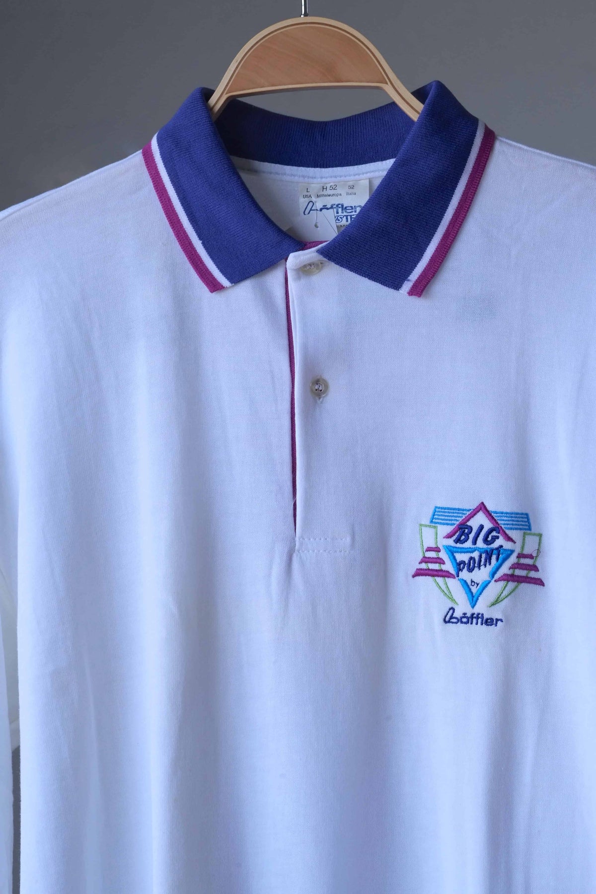 Close-up of royal purple collar with magenta and white tipping, two-button placket and embroidered Big Point logo on a white Löffler polo