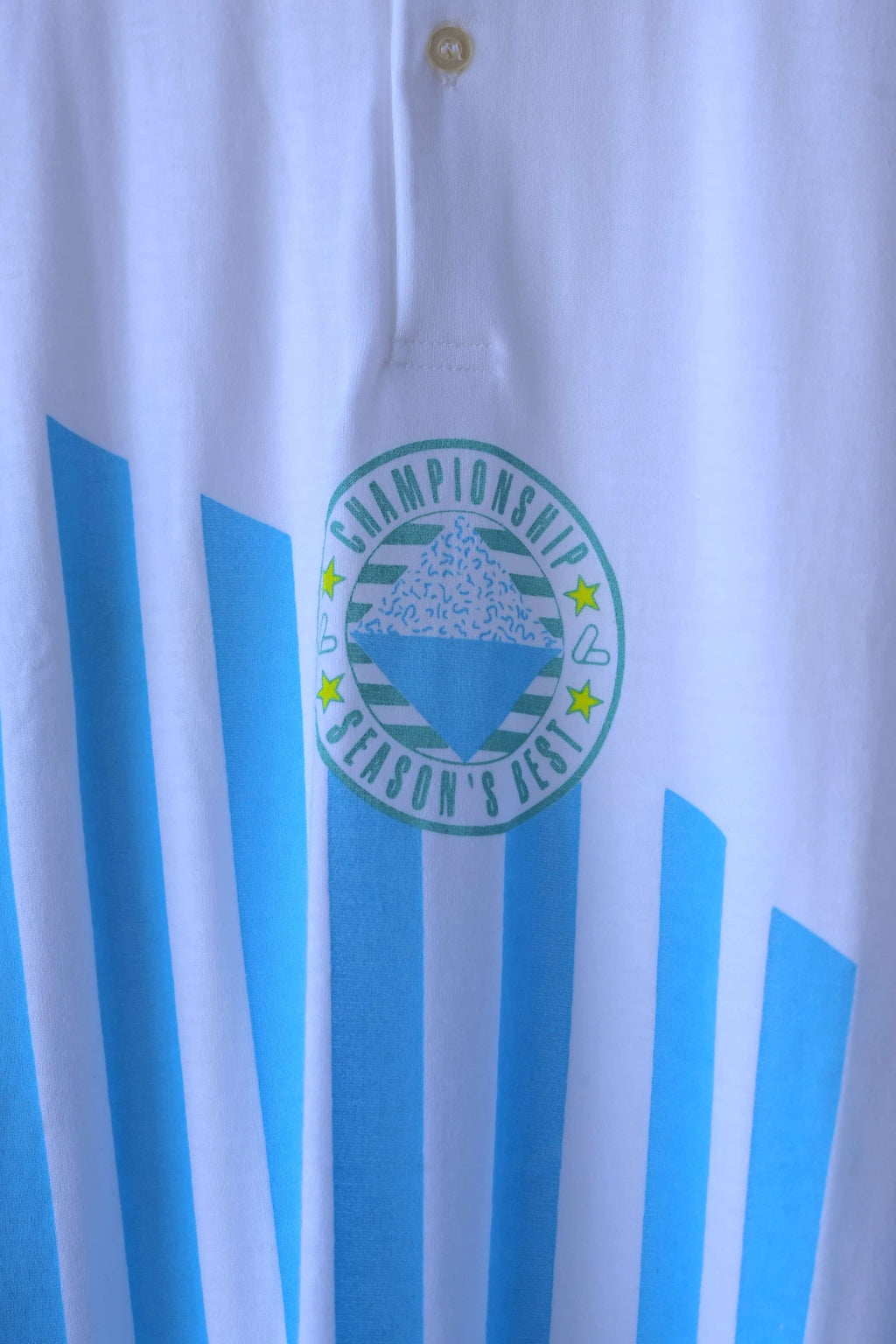 Close-up of Löffler polo collar, two-button placket and sky blue Championship Season’s Best badge over pink stripes