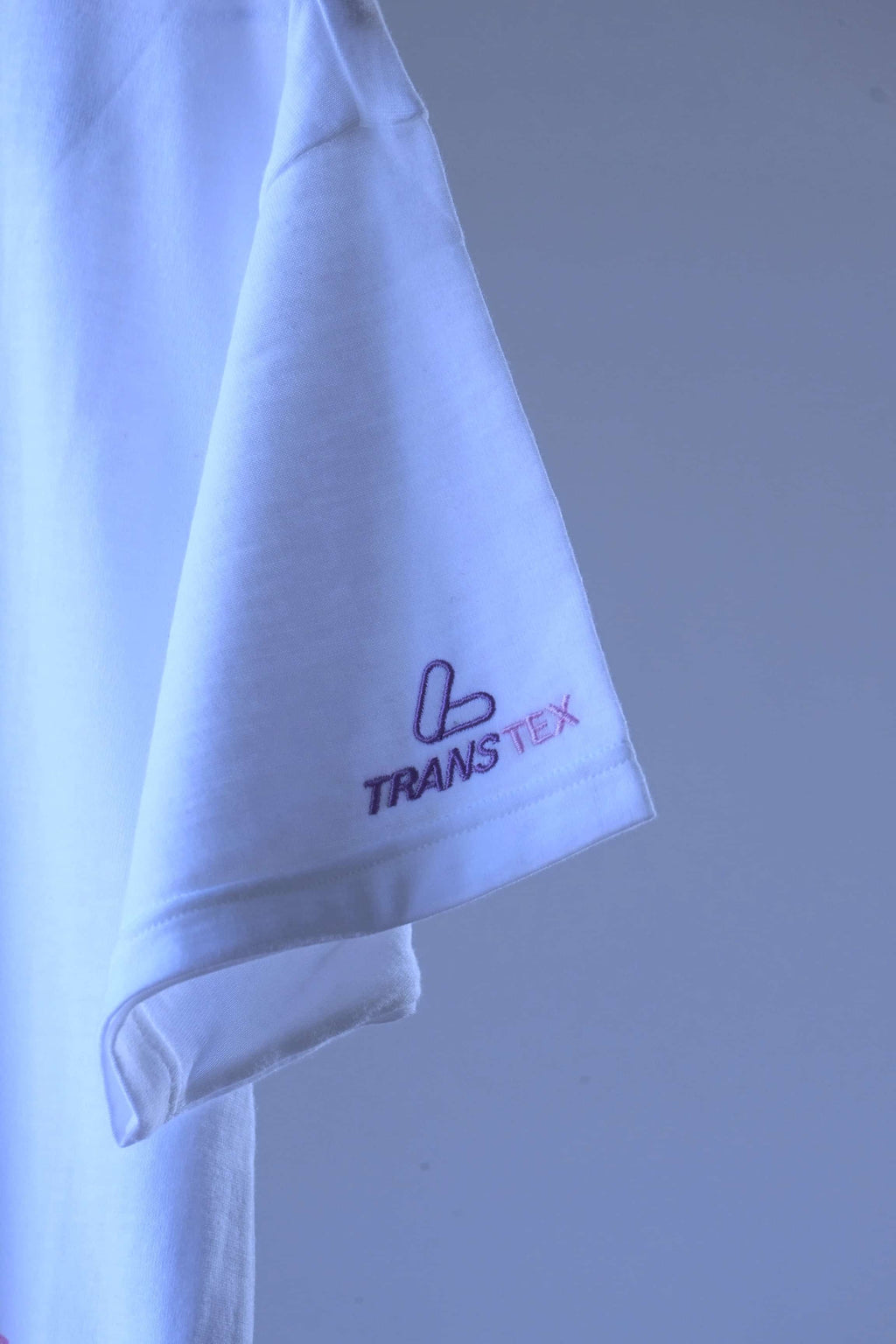 Close-up of purple and pink embroidered Transtex logo on the sleeve of a white Löffler 90s polo