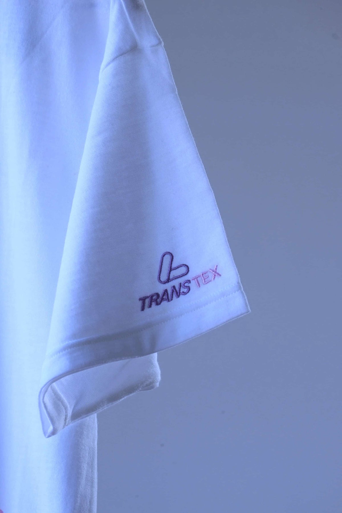 Close-up of purple and pink embroidered Transtex logo on the sleeve of a white Löffler 90s polo