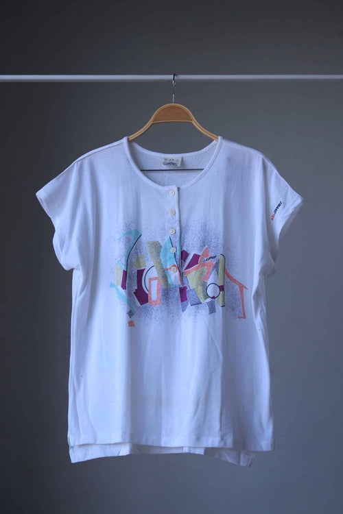 Front view of white Löffler 90s women’s henley top with cap sleeves, round neckline, five-button placket and Memphis-style graphic over a speckled spray print