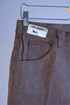 Close-up of the waistband and front pocket of the heather brown Lee Leens, showing the original paper size tag 34x31 and the 'Lee Leens' cloth label.
