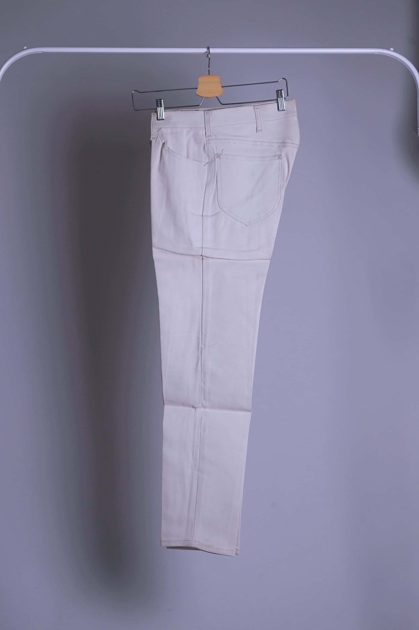 NOS Vintage Lee Leens Lastic Stretch trousers in beige color, folded, hanging on a metal rack.