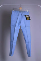 Back view of NOS 70s Lee Leens Lastic Stretch denim trousers in light sky blue, shown hanging on a rack with original black and yellow 'Lastic Lee' paper tag.