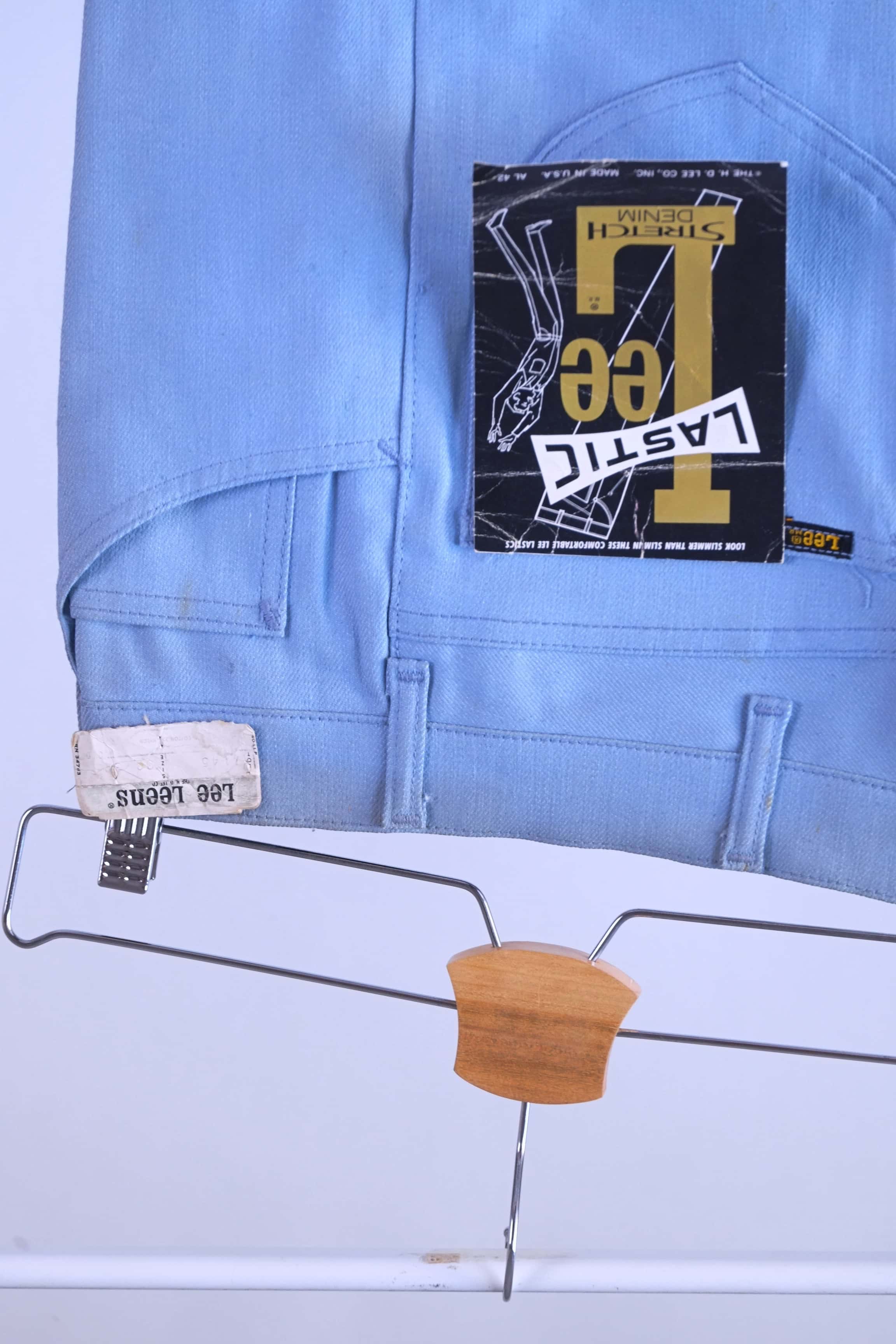 Close-up detail shot of the back of the NOS 70s Lee Leens in light blue, showing the original white 'Lee Leens' label and the black, yellow, and red 'Lastic Lee Stretch Denim' product hang tag.