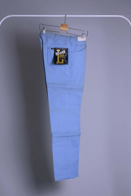 NOS 70s Lee Leens Lastic Stretch denim trousers in light sky blue, shown hanging on a rack with original black and yellow 'Lastic Lee' paper tag and 'Lee Leens' cloth label attached.
