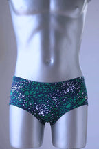 A plastic mannequin wearing a pair of Green swim briefs with an abstract leopard print pattern. The pattern includes shades of green, black, and white.
