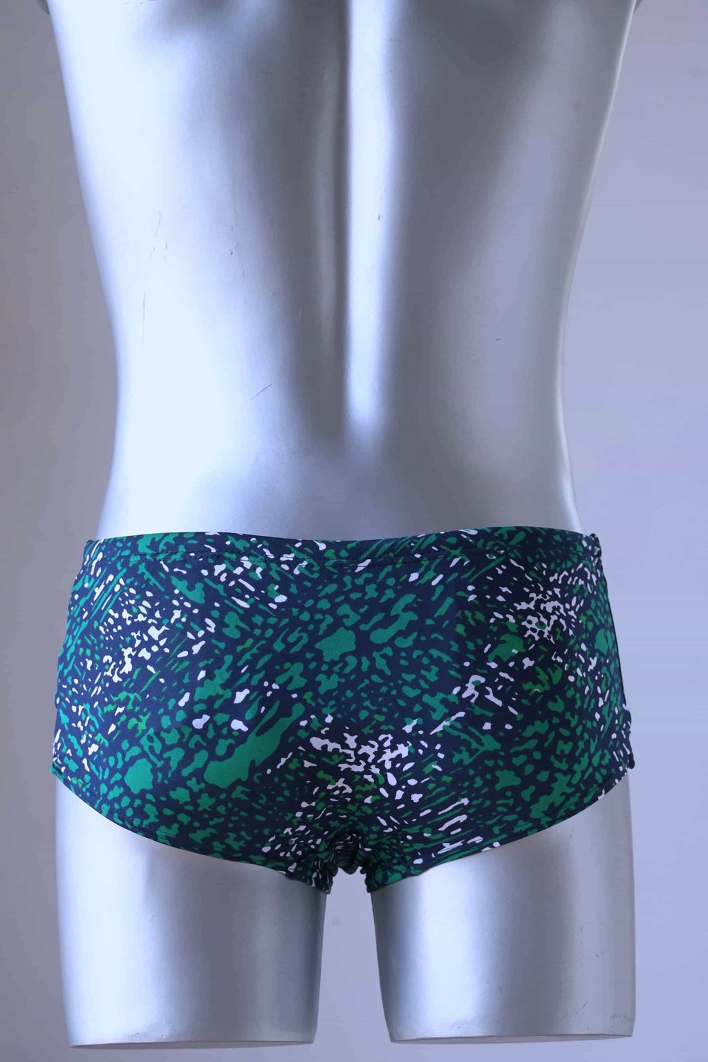 Back view shot of A plastic mannequin wearing a pair of Green swim briefs with an abstract leopard print pattern. The pattern includes shades of green, black, and white.