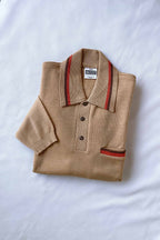 Folded beige pure new wool knit polo shirt with orange and brown striped collar detailing flat-laid on a white background.