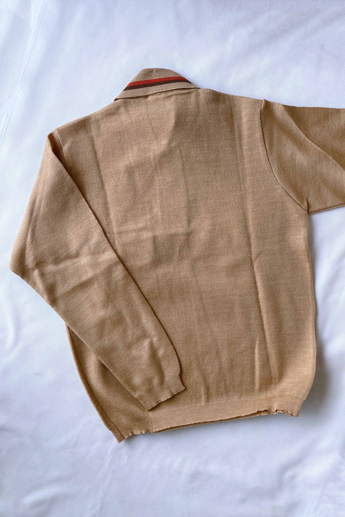 The back of a beige pure new wool knit polo sweater with orange and brown striped collar detailing flat-laid on a white background.