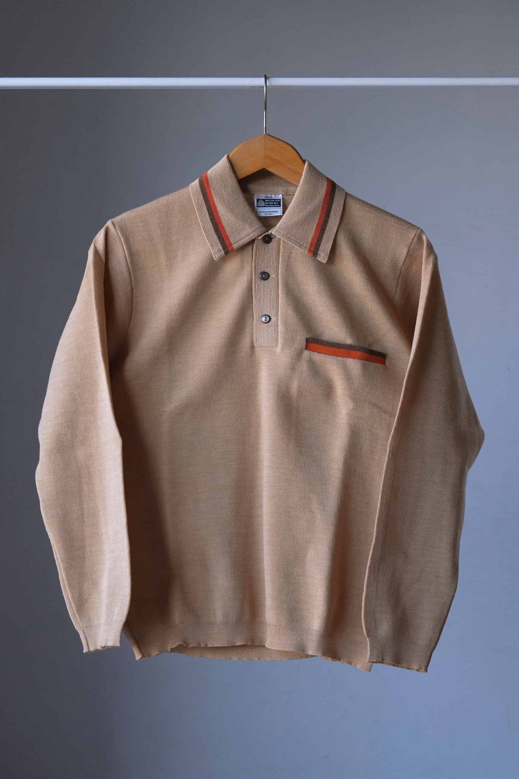 Full front view of a vintage beige long-sleeve wool knit polo sweater on a wooden hanger against a gray background.