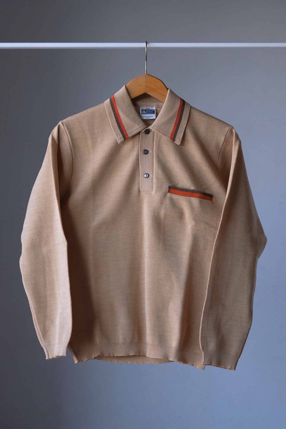 Full front view of a vintage beige long-sleeve wool knit polo sweater on a wooden hanger against a gray background.