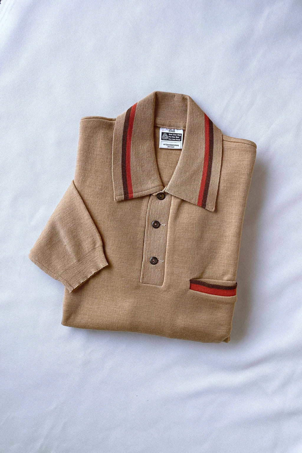 Folded beige pure new wool knit polo sweater with orange and brown striped collar detailing flat-laid on a white background.