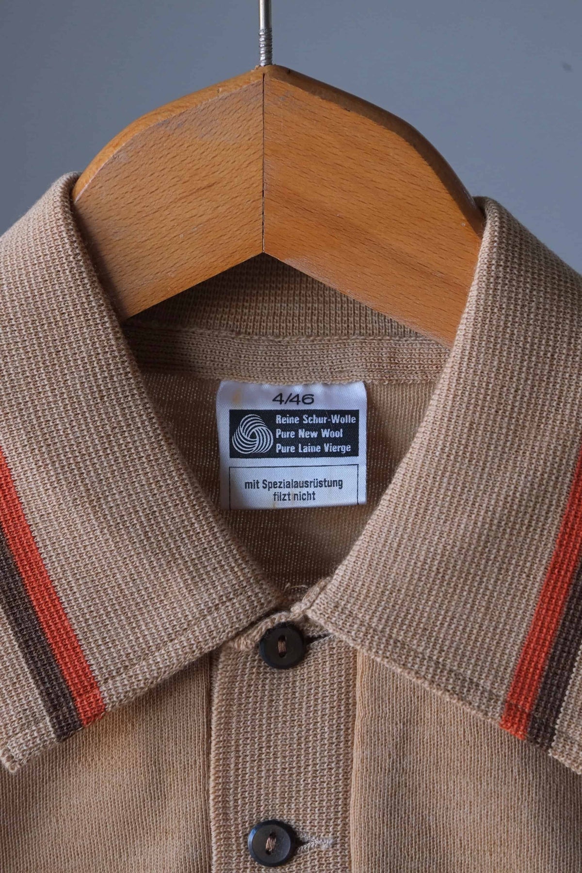 Close-up shot of the collar, buttons, and Woolmark pure new wool tag on a vintage beige knit polo sweater.