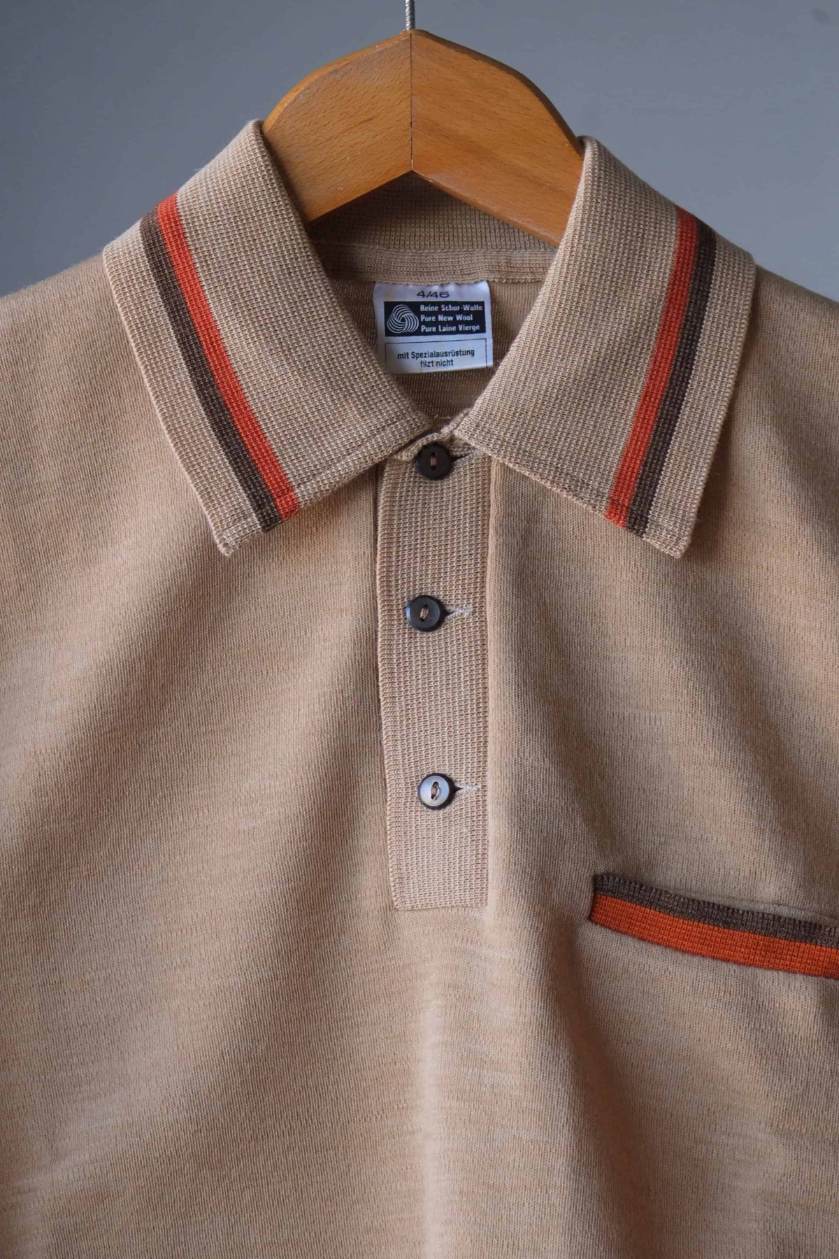 Mid-section detail shot of a vintage beige knit polo shirt showing the striped collar tipping, button placket, and chest pocket.