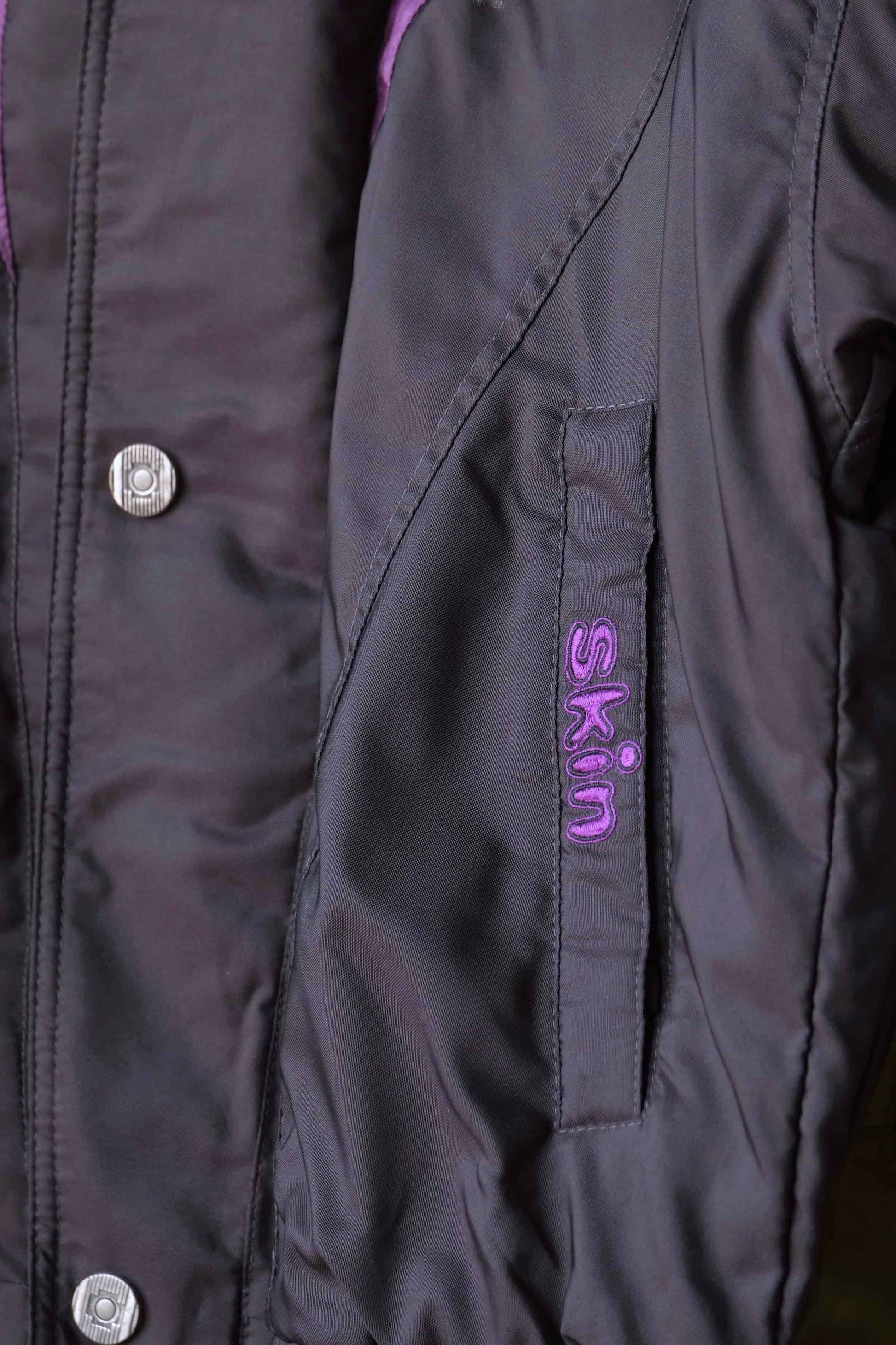 Close up of the stitched Skin logo on the front pocket of the Vintage Men's 90's Ski Jacket in black purple
