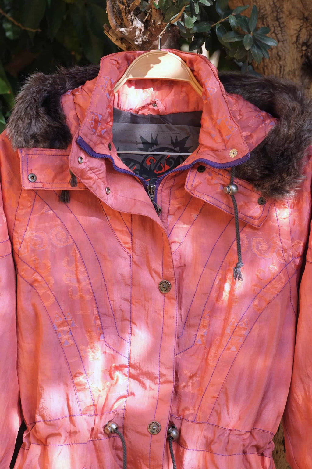 Close view of a coral colored Vintage 90's Women's Ski Jacket hanging on a tree with some sun rays